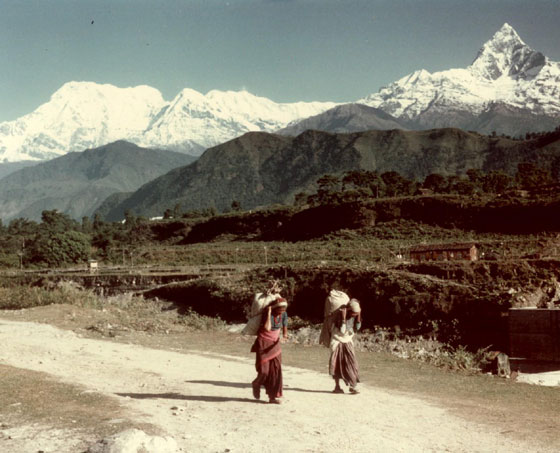 Nordwestlich von Pokhara (Nepal): Blick auf den Annapurna-Südgipfel (7195 m) und den Annapurna I (8078 m) links und den Machhapuchhare (6997 m) rechts. Im Vordergrund zwei Frauen, die Lasten mit dem typischen Stirnband tragen.  / Photo D.S. Herbst 1982
